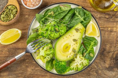 Brokolili vejetaryen yeşil salata, avokado, marul ve tohumlar ahşap arka planda, temiz yemek, diyet, vejetaryen gıda konsepti, üst görünüm.,