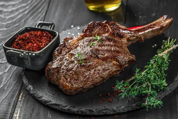 Tomahawk rib beef steak with spices and herbs on a dark background. top view. copy space for text.
