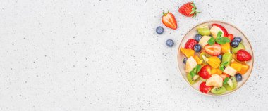 Hafif arka planda sağlıklı taze meyve salatası, kivi, muz, çilek, limon, yabanmersini ve portakal, üst manzara. Boşluğu kopyala