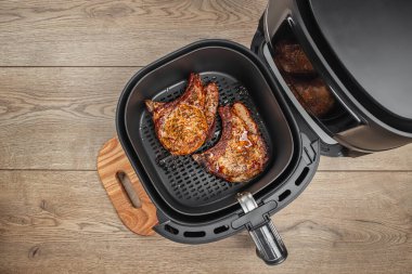 Ahşap arka planda, hava kızartma fırınından ızgara biftekler, sepetin içinde sıcak hava dolaşarak az yağlı ya da hiç yağsız gevrek yiyecekler..