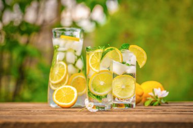 Yaz ferahlatıcı limonata, buzlu içecek ve bahçede masada limon dilimleri. Taze, sağlıklı, soğuk limon suyu. Boşluğu kopyala.