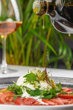 Taze burrata ve domates salatası üzerine zeytinyağı serpiştirmek. Öğlen veya akşam yemeği için lezzetli ve sağlıklı yemekler.
