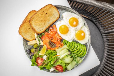 Yumurtalı sağlıklı kahvaltı tabağı, füme somon, avokado, tost ve taze salata. Lezzetli dengeli gıda konsepti. en üstteki görünüm.