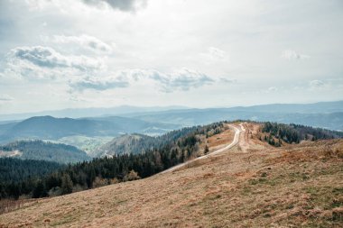 Dönek dağ yolu bulutlu bir gökyüzünün altında manzaralı tepeler boyunca uzanıyor..