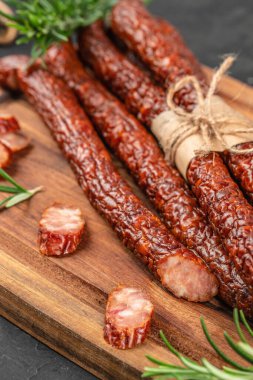 Ahşap bir kesme tahtasının üzerinde servis edilen bitkilerle tütsülenmiş sosisler..