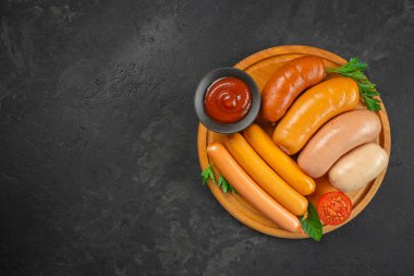 Farklı sosisler, ketçap ve siyah arka plandaki ahşap tabakta taze otlar. Üst Manzara. Boşluğu kopyala.