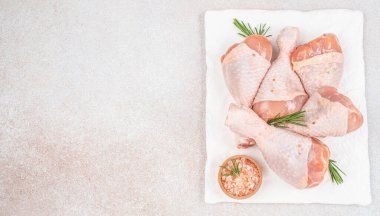 Beyaz seramik tabakta çiğ tavuk budu, biberiye ve pembe tuz. Uzun afiş biçimi. Üst Manzara. Boşluğu kopyala.