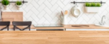 Ahşap mutfak tezgahı odaklı ve arka plan elementleri bulanık. Mutfak tezgahları, sandalyeler, bitkiler ve beyaz fayans duvarları rahat bir pişirme alanı oluşturuyor..