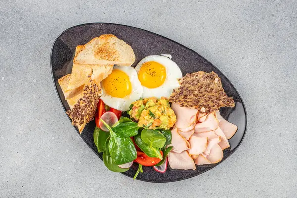 Sağlıklı kahvaltı tabağı, güneşli yan yumurtalar, avokado püresi, yeşiller, hindi dilimleri ve tost.