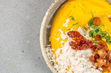 Üzerinde rendelenmiş peynir, kavrulmuş domates, gevrek domuz ısırıkları ve taze otlar bulunan canlı bir kase kremalı sarı polenta rahatlatıcı ve renkli bir yemek sunar.