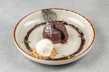 Çikolata sosu, kurabiye kırıntıları, nane yaprakları ve pudra şekeriyle süslenmiş bir top vanilyalı çikolatalı lav keki.