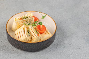 Taze sebze ve otlarla dolu ızgara tortilla paketleri. Çeri domatesli ve mikroyeşillikli modern bir kasede servis ediliyor..