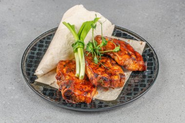 Izgara domuz pirzolası taze yeşil soğan ve siyah seramik tabakta düz ekmek ile servis edilir..