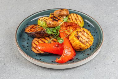 Mısır, patlıcan, kabak, biber, domates ve mantar içeren renkli bir sebze karışımı. Mavi seramik tabakta mikro yeşilliklerle süslenmiş..