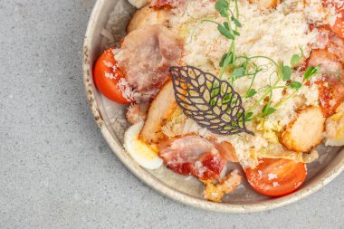 Izgara tavuklu taze Sezar salatası, çıtır pastırma, vişneli domates, haşlanmış yumurta, üstüne de mikroyeşillik ve dekoratif garnitürle parmesan peyniri..