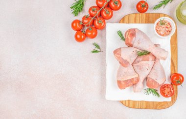 Çeri domatesli, pembe tuzlu ve biberiyeli ahşap kesme tahtasındaki çiğ tavuk budu pişirmeye ve baharata hazırdır..