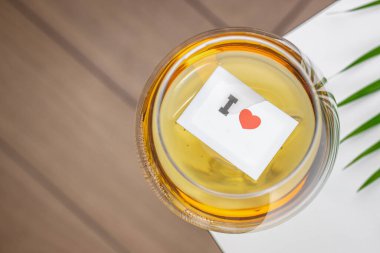 İçinde aşk sembolünün yüzdüğü, romantik ve neşeli bir atmosfer yaratan küçük bir kağıt parçasıyla bir kadeh beyaz şarabın yakın çekim görüntüsü..