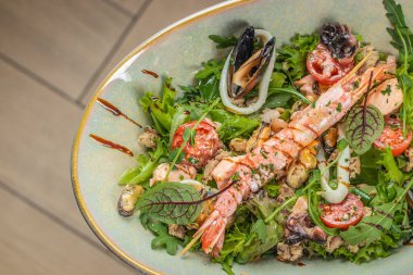 Izgara karides, midye, kalamar, kiraz domatesleri, taze yeşillikler ve seramik kasede güzelce yerleştirilmiş balzamik jöle içeren canlı bir deniz ürünleri salatası..