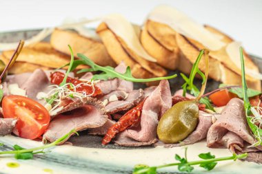 Kavrulmuş biftek carpaccio, kızarmış ekmek, güneşte kurutulmuş domates, kapari, parmesan talaşı, taze yeşillik ve kremalı soslu vişneli domates..