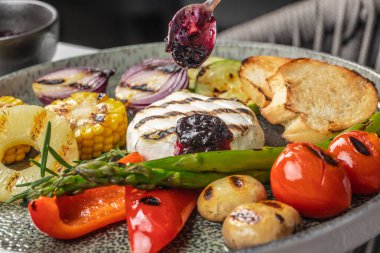 Renkli bir ızgara sebze tabağı kremalı peynirli, üzerine kaşık dolusu böğürtlen sosu, kızarmış ekmek ve taze otlarla servis edilmiş..