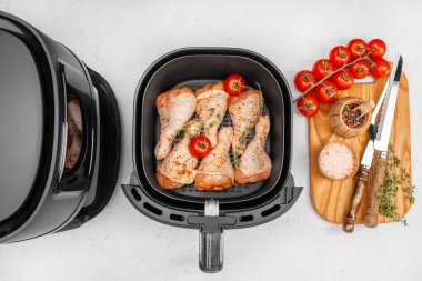 Taze domatesli çiğ tavuk budu ve otlar, baharatlar, sarmaşıkta kiraz domatesleri ve ahşap bir tahtanın üzerinde kırsal mutfak aletleri ile çevrili bir hava kızartma sepetinde düzenlenir..