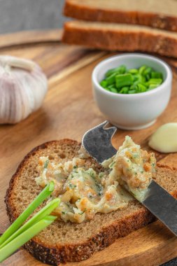 Bir dilim çavdar ekmeği cömertçe sarımsaklı domuz yağıyla kaplanır ve yeşil soğanlarla süslenir, ahşap bir tahtanın üzerinde taze malzemelerle çevrelenir..