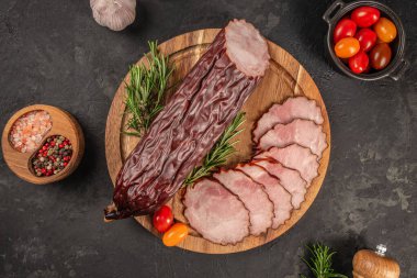 Dilimlenmiş kuru et, ahşap bir tahtada zarif bir şekilde düzenlenir. Taze biberiye, kiraz domatesleri, tuz ve karabiber ile birlikte. Köy ve lezzetli bir şarküteri sunumu için..