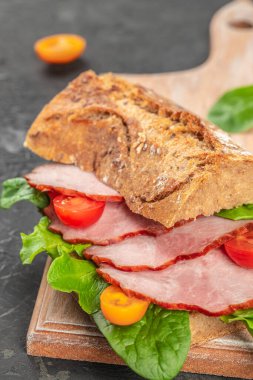 Kabuklu tam tahıllı ekmekten yapılmış, füme domuz eti, taze ıspanak yaprakları ve ahşap bir tahtanın üzerindeki renkli domateslerle katmanlanmış bir köy sandviçi.