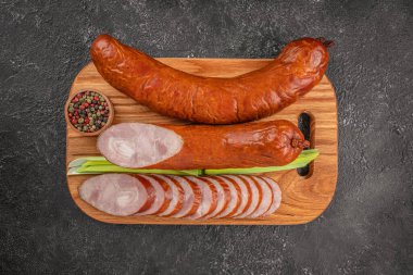 Füme domuz sosisi dilimlenmiş ve ahşap bir kesim tahtasının üzerinde servis edilmiş yeşil soğanlı ve koyu dokulu arka planda bir kase karışık biberli..