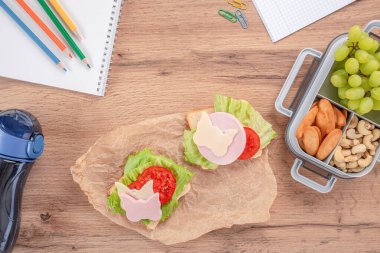 Kelebek biçimli peynir ve jambonla süslenmiş açık sandviçlerle yaratıcı okul yemeği, ahşap bir masanın üzerinde üzüm, fındık ve krakerlerin yanında servis edilir..