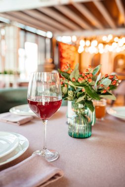 Zarif bir restoran masası, bir bardak kırmızı şarap ve sıcak ortam aydınlatmalı bir çiçek süsü..