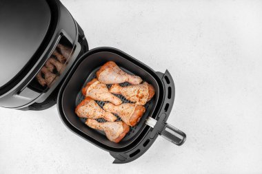 Çiğ baharatlı tavuk budu, temiz beyaz mutfak tezgahında pişirilmeye hazır, siyah bir fritözün sepetinde güzelce düzenlenir..