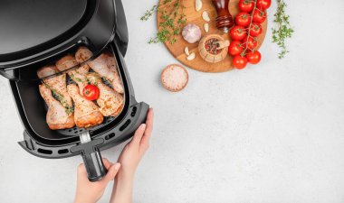 Çiğ salamura edilmiş tavuk budu, otlar ve kiraz domatesleri, mutfak tezgahında sarımsak, tuz ve biber gibi taze malzemelerle çevrili bir hava kızartma sepetinde düzenlenir..