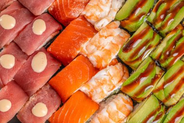 Çeşitli suşi rulolarının genel görünümü renkli sıra dizilmiş canlı ton balığı, somon, karides ve avokado soslarını ön plana çıkarıyor..