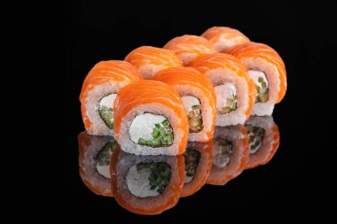 Tertemiz sıralanmış suşi ruloları krem peyniri, salatalık ve taze somonla kaplı mükemmel yansıması olan parlak siyah bir yüzey üzerinde sergilenir..
