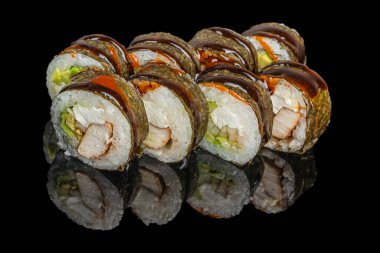 Suşi, tavuk, krem peynir, avokado ve deniz yosununa sarılı ve koyu soslu sebzeler yansıtıcı siyah bir yüzeye güzelce yerleştirilmiştir..