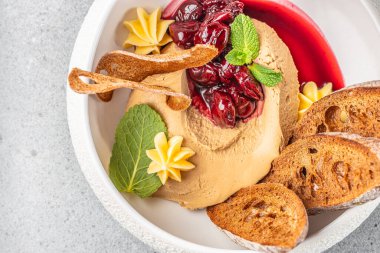 Kremalı ezme zarif bir şekilde vişne ezmesi, kızarmış baget dilimleri, çırpılmış tereyağı ve taze nane ile servis edilir..