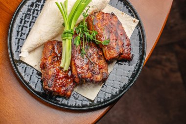 Barbekü domuz pirzolası ve siyah seramik tabakta yeşil soğanlı garnitür..