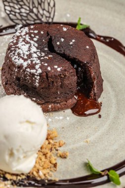 Klasik çikolatalı lav keki, zengin erimiş merkezi pudra şekeriyle kaplanmış ve bir kepçe vanilyalı dondurma ve parçalanmış fındıkla servis ediliyor..