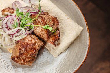 Izgara et parçaları ince düz ekmek, taze soğan halkaları ve kırsal seramik tabakta mikro yeşillikler ile servis edilir..