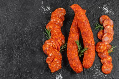 Koyu dokulu arka planda biberiye filizi ile hazırlanmış füme sosis ve dilimlenmiş baharatlı salam. Üst görünüm.