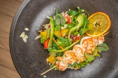 Izgara karides şişleri taze karışık sebzeler, canlı sebzeler ve narenciye dilimleri üzerine servis edilir. Renkli ve ferahlatıcı deniz ürünleri salatası yaratır..