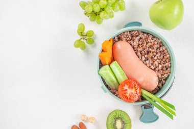 Karabuğday, sosis, taze sebze ve meyvelerden oluşan dengeli bir yemek renkli ve sağlıklı bir sunum üst görüşü olan bir beslenme çantasında düzenlenir. Boşluğu kopyala.