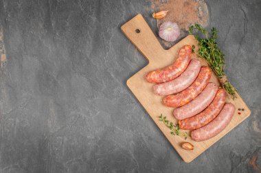 Sarımsaklı çiğ domuz sosisi ve ahşap bir tahtanın üzerinde siyah taştan bir arka planda otlar. Boşluğu kopyala, üst görünüm.