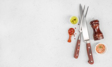 Biberli mutfak bıçakları, pembe tuz, zeytinyağı ve hafif arka planda biber öğütücü. Boşluğu kopyala, üst görünüm.