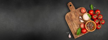 Köy ahşap kesim tahtası taze domatesler, otlar, sarımsak, tuz ve siyah arka planda biber. Uzun afiş biçimi. Üst Manzara. Boşluğu kopyala