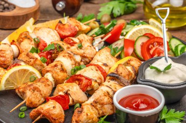 Kızarmış tavuk şişleri ve sebzeler yanında taze soslar ve ahşap bir masada dilimlenmiş salata..