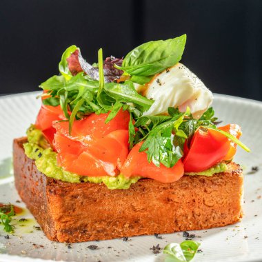 Avokado soslu gurme tostu, füme somon, kiraz domatesleri, karışık yeşillikler ve beyaz tabakta haşlanmış yumurta..