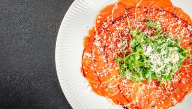 İnce dilimlenmiş somon carpaccio rendelenmiş peynir, roka ve beyaz seramik tabakta balzamik jöle serpiştirilmiş. Üst Manzara. Boşluğu kopyala.