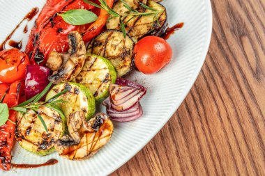 Taze otlar ve balzamik jöleli rengarenk bir sebze karışımı ahşap bir masanın üzerindeki beyaz seramik bir tabakta ustalıkla düzenlenir. Üst Manzara. Boşluğu kopyala.